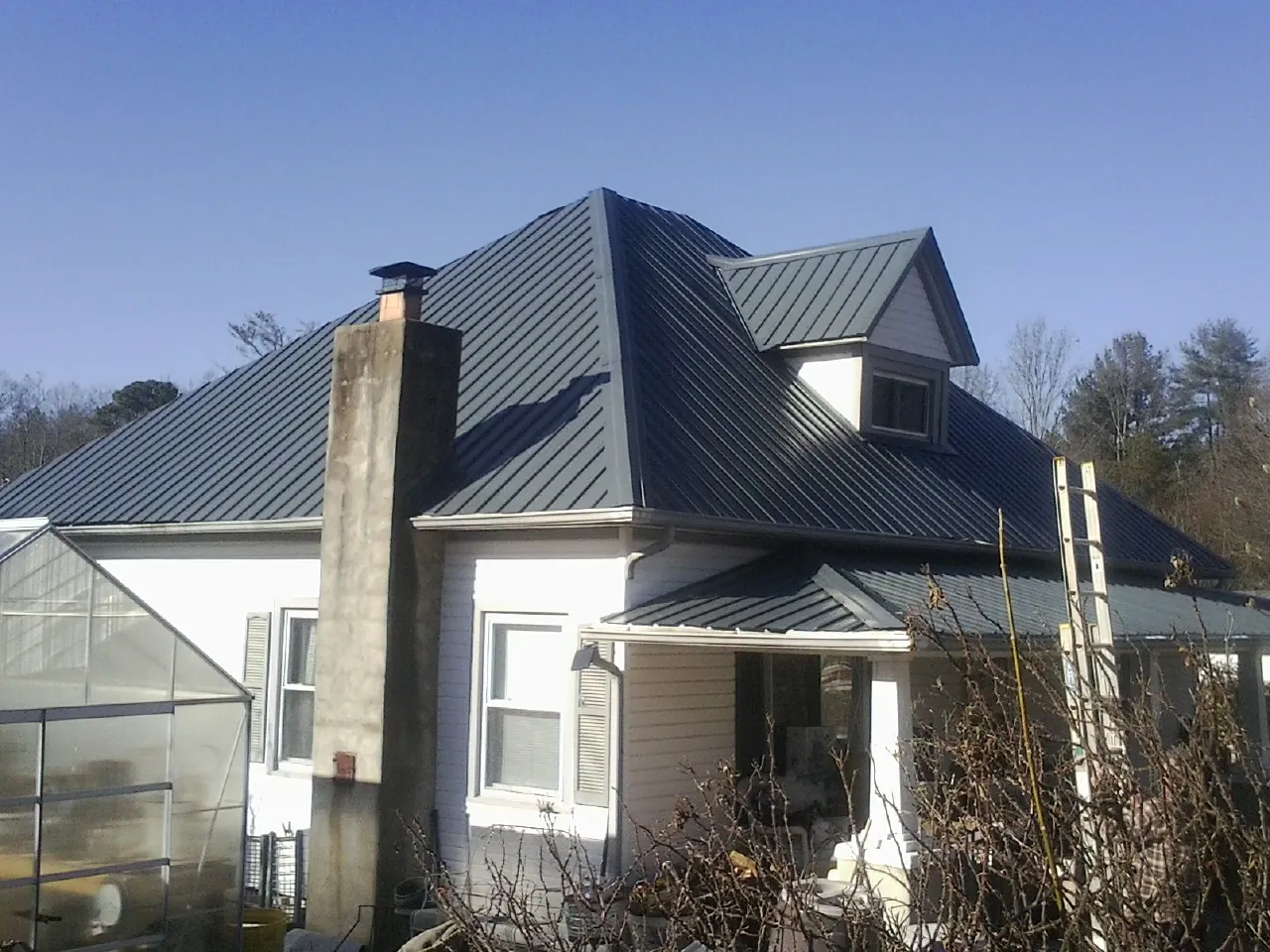 Dark blue standing seam metal roof on a white farmhouse with dormer — Slate & Tile Roof Repair by Roofing Brothers in Braddock