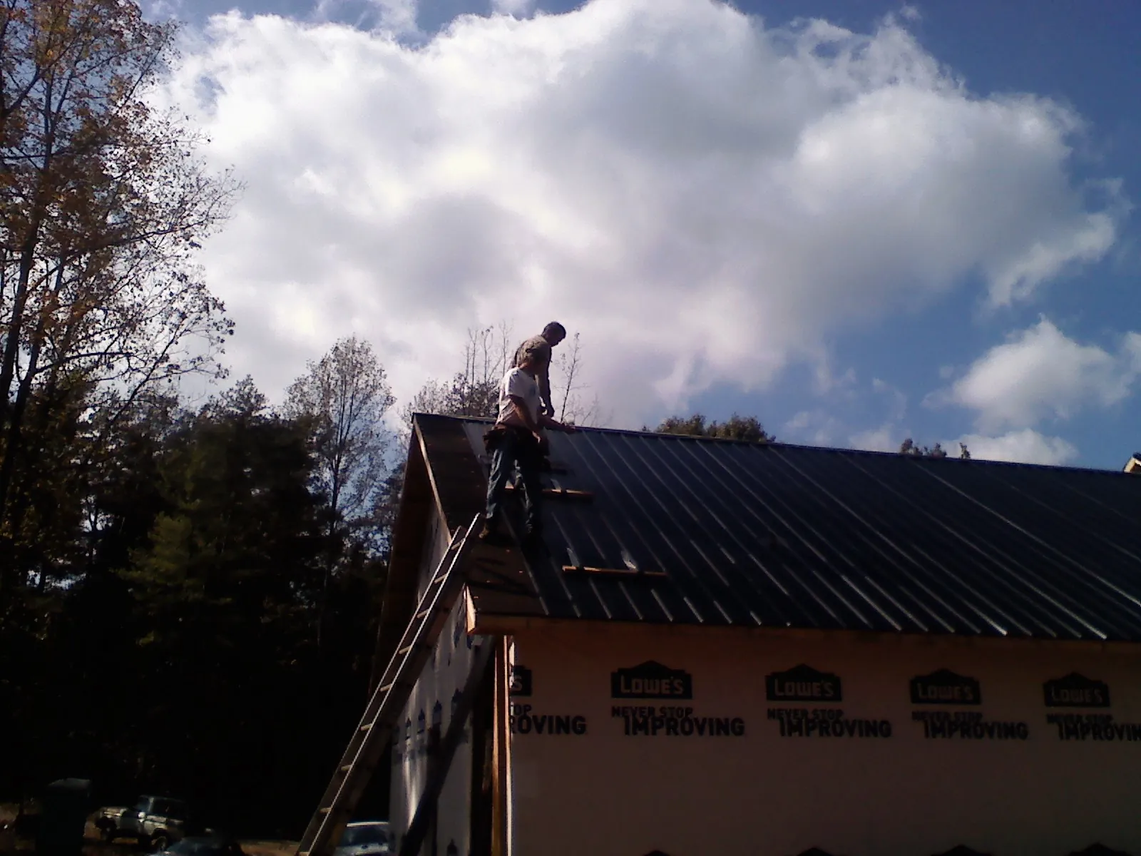 Roofer fastening dark metal panels high against a cloudy sky, from a Roof Inspection job in Braddock