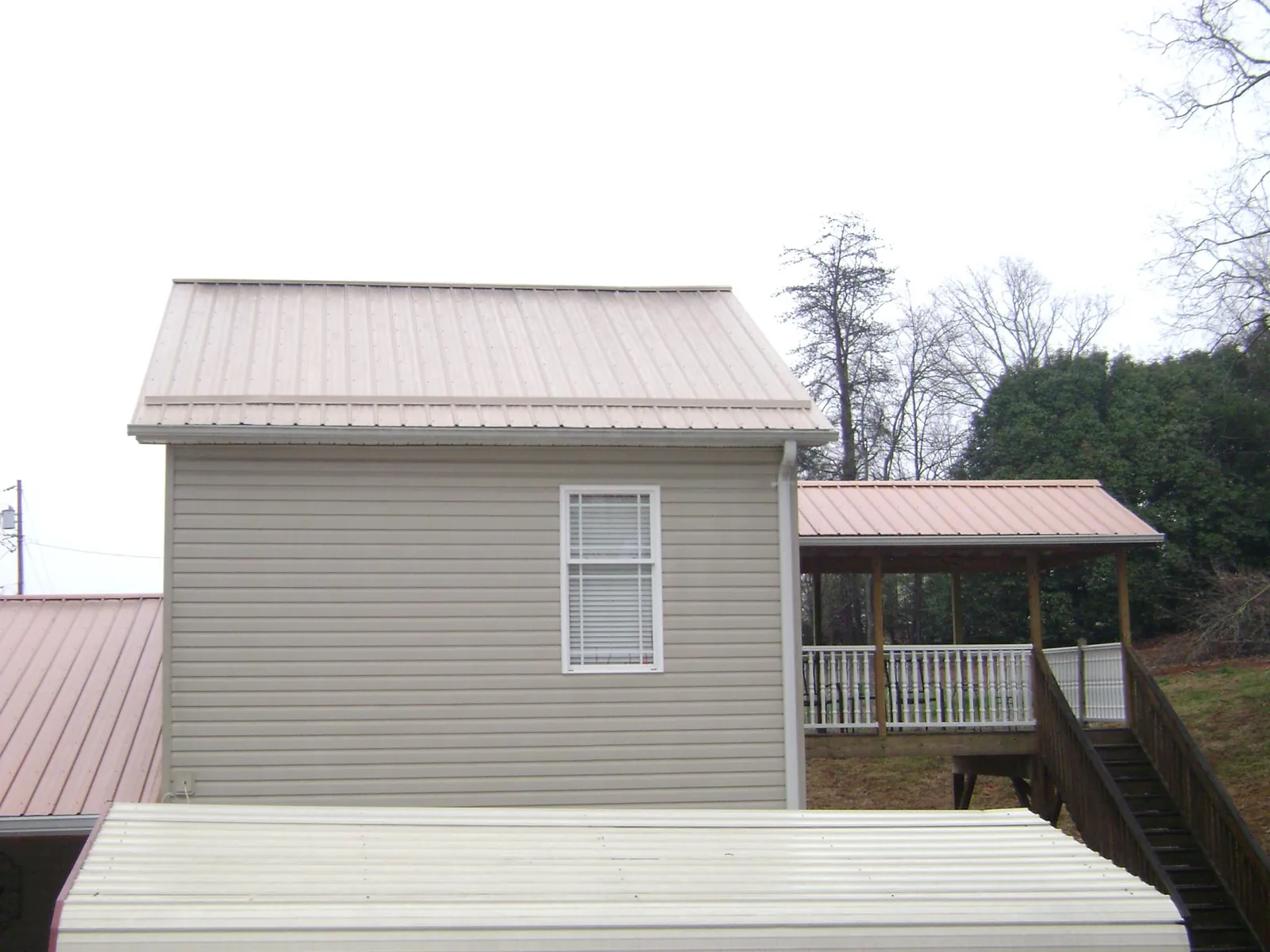 Tan metal roofs on a two story addition and attached porch, from a Roof Replacement job in Braddock